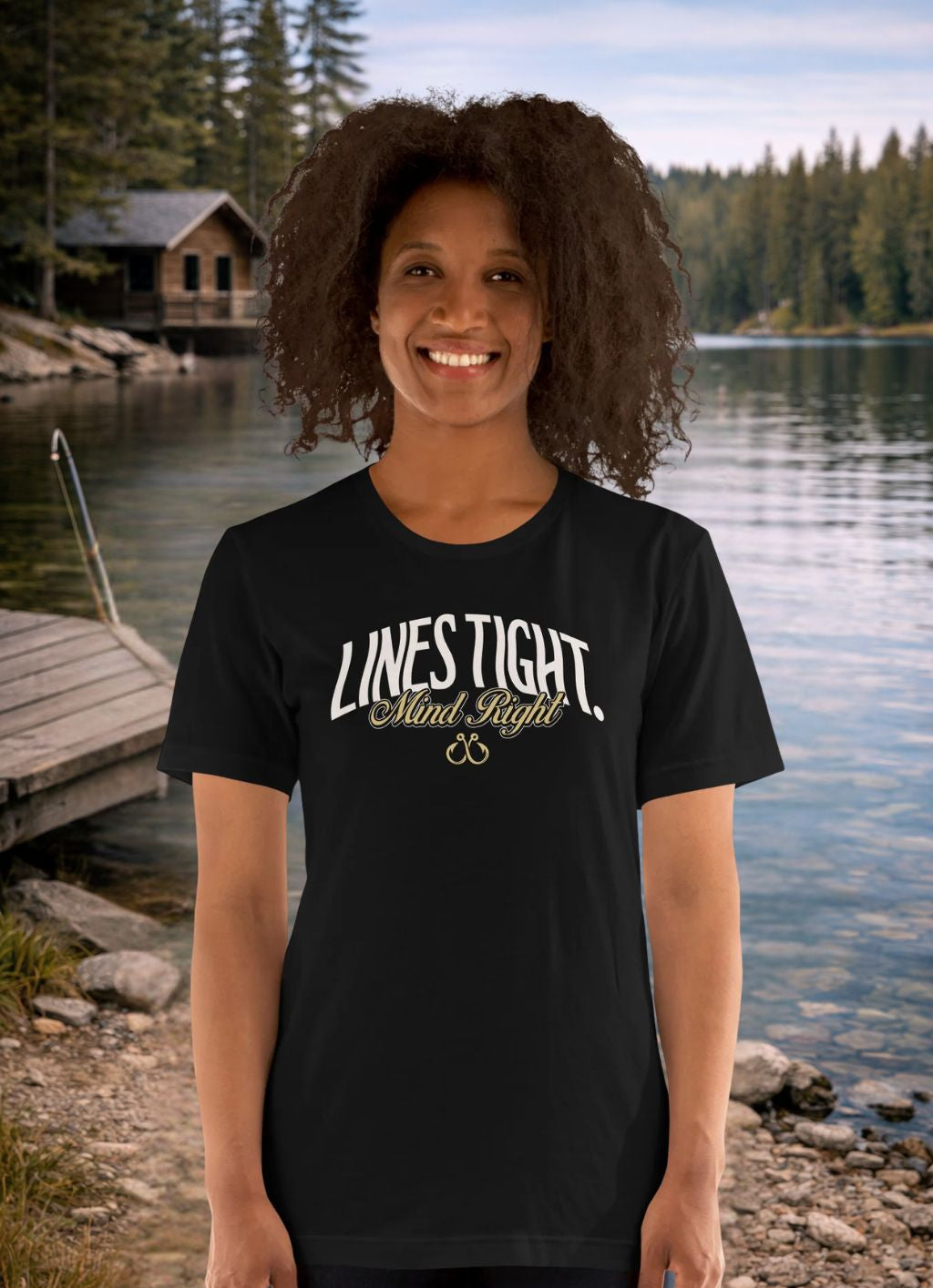 Person wearing a black t-shirt with 'Lives Tight, Minds Light' text by a lake with a cabin in the background.
