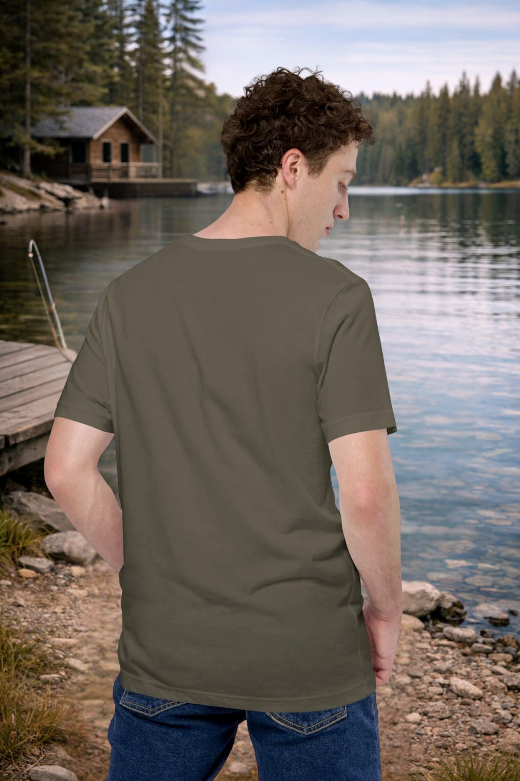 Man wearing a green t-shirt by a lake with a cabin in the background