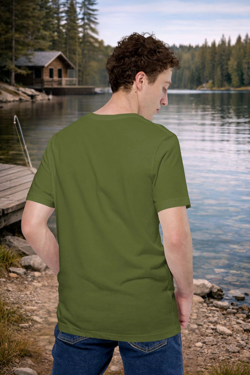Man wearing a green t-shirt by a lake with a cabin in the background