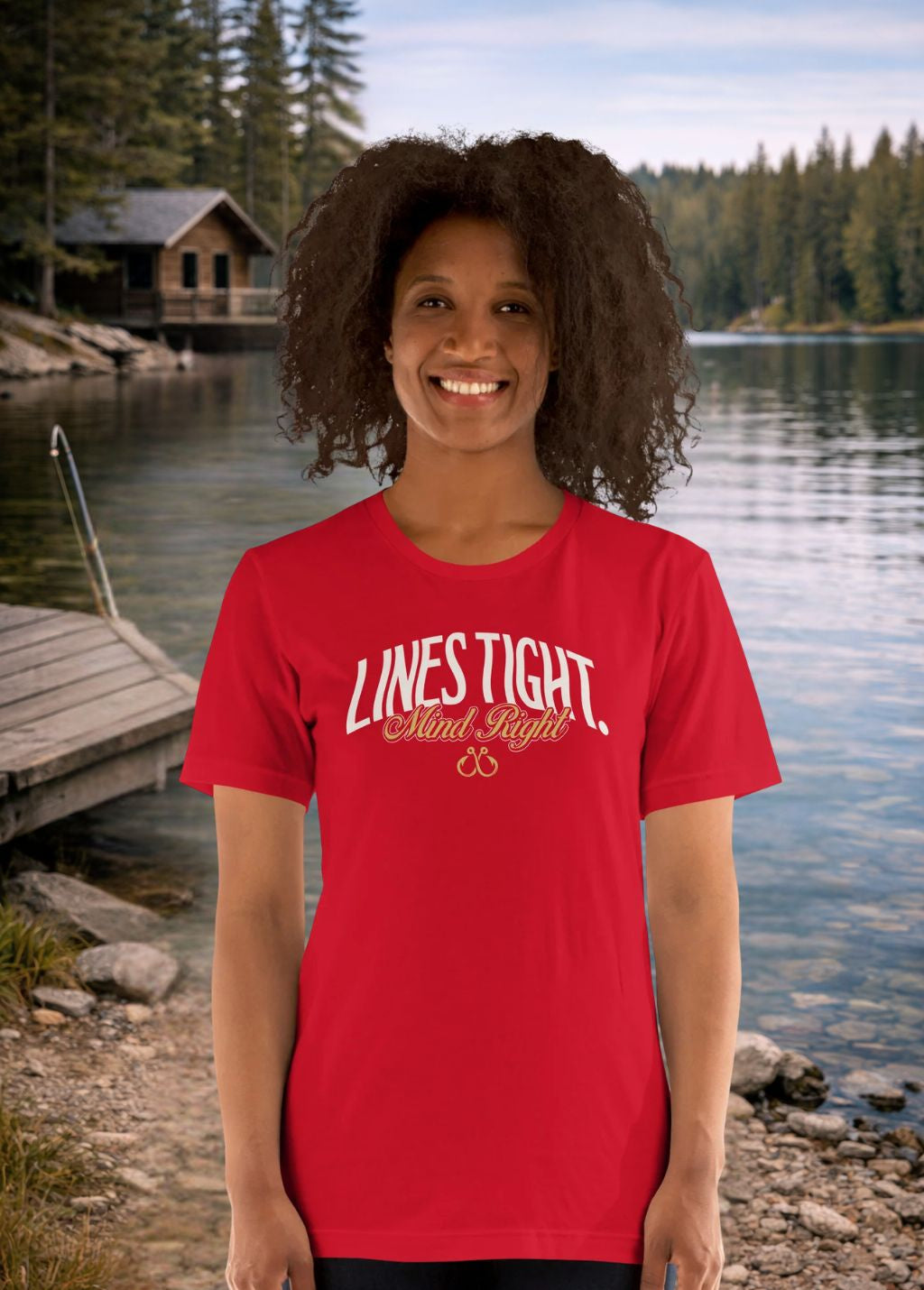 Person wearing a red fishing t-shirt with 'LINES TIGHT. Mind Right.' text by a lake with a cabin in the background.